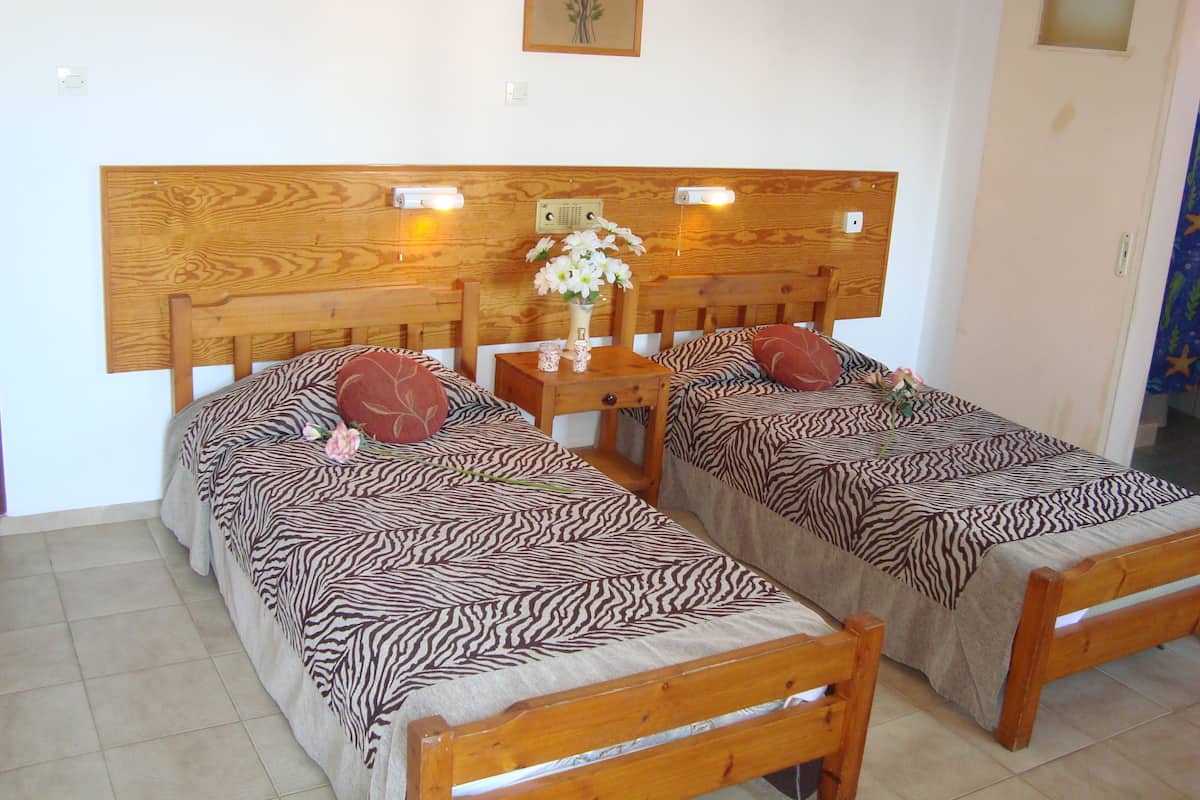 Una habitación con dos camas de madera, ropa de cama con estampado de cebra, una mesita de noche con un florero y una lámpara de pared.