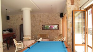 A pool table in a room with stone walls, a window, and a door leading outside. - Arkadi Apartments by Checkin (Hersonissos)