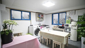 Une cuisine compacte équipée d’un lave-linge, d’un four à micro-ondes et d’une table à manger recouverte d’une nappe rose.