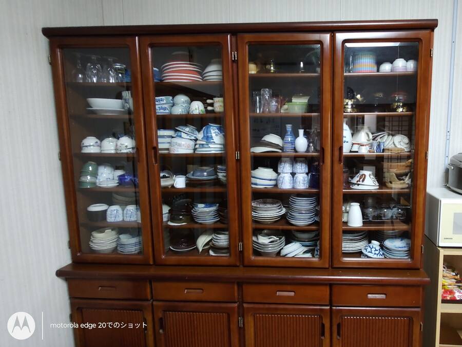 A wooden cabinet with glass doors containing various dishes and kitchenware.