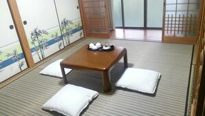A traditional Japanese room with tatami flooring, a low wooden table with a tray of teaware, and white cushions. - Guest House Nakamura House (Oki)