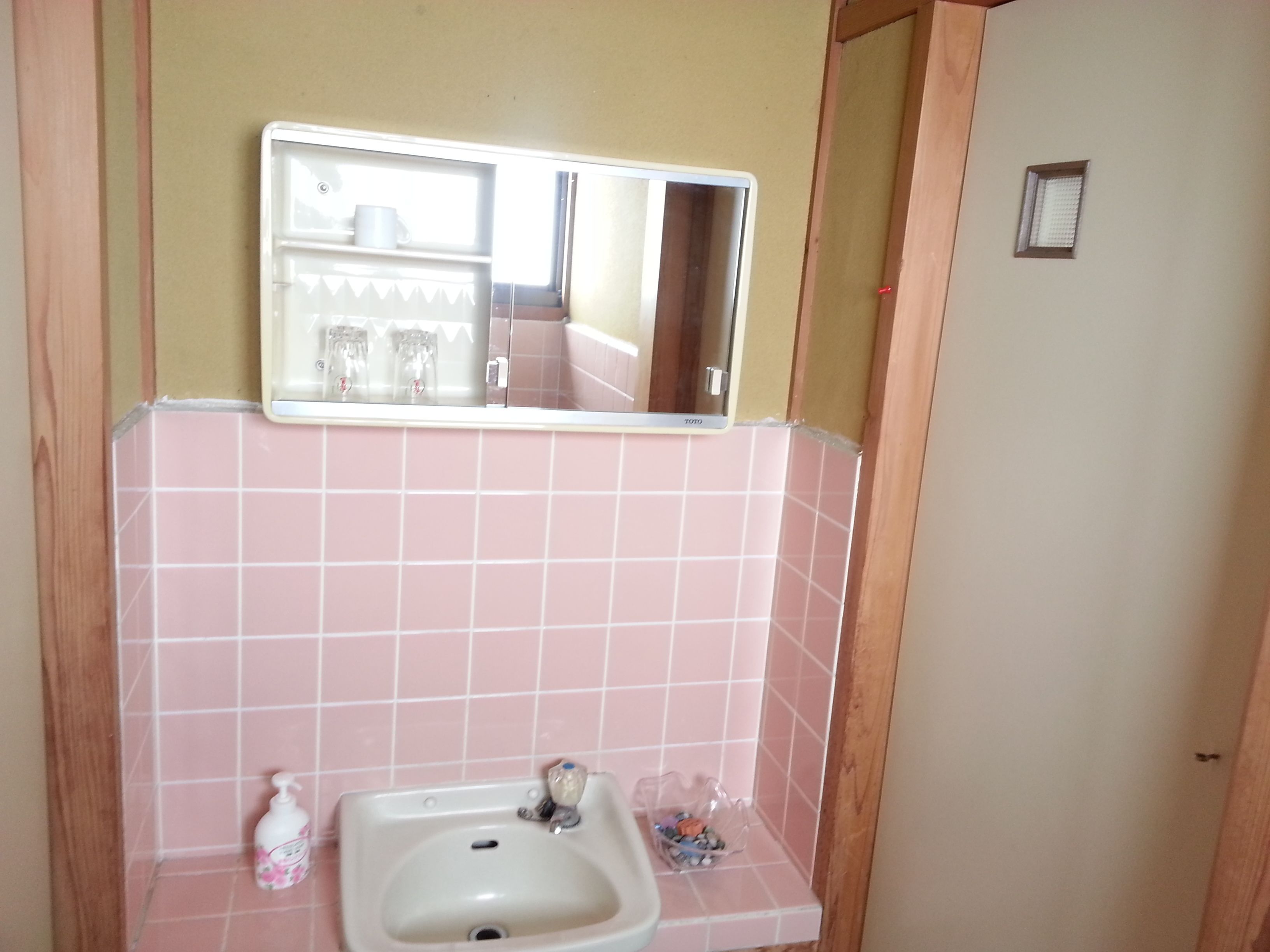 A bathroom with pink tiles, a sink, a mirror, and a small window.