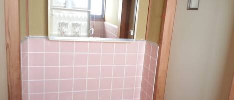 A bathroom with pink tiles, a sink, a mirror, and a small window.