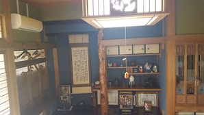 A traditional Japanese room with tatami flooring, a shoji screen, a hanging lantern, and a shelf with various decorative items. - Guest House Nakamura House (Oki)