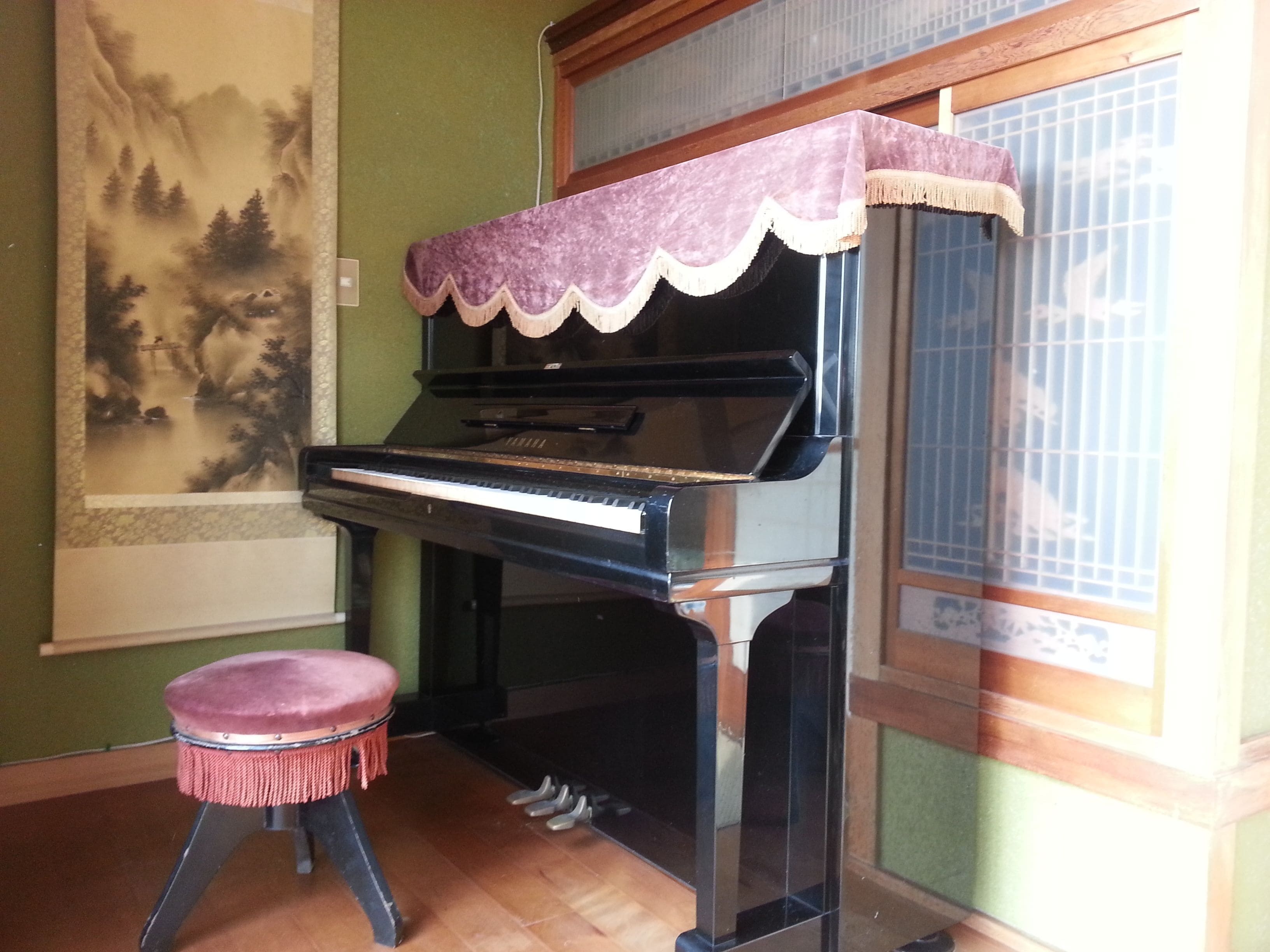Un piano recouvert d’une housse violette, un tabouret et un tableau accroché au mur.