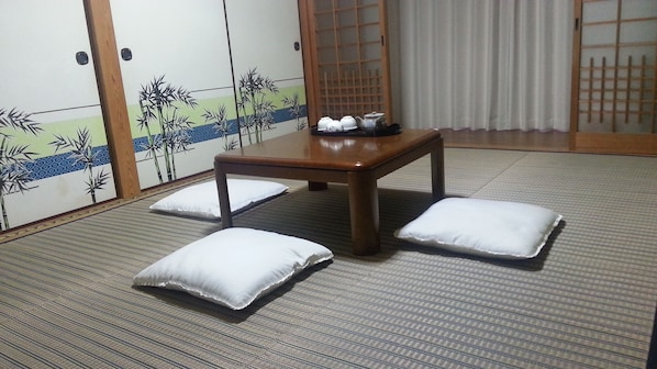 A traditional Japanese room with tatami flooring, a low wooden table, and white cushions. - Guest House Nakamura House (Oki)