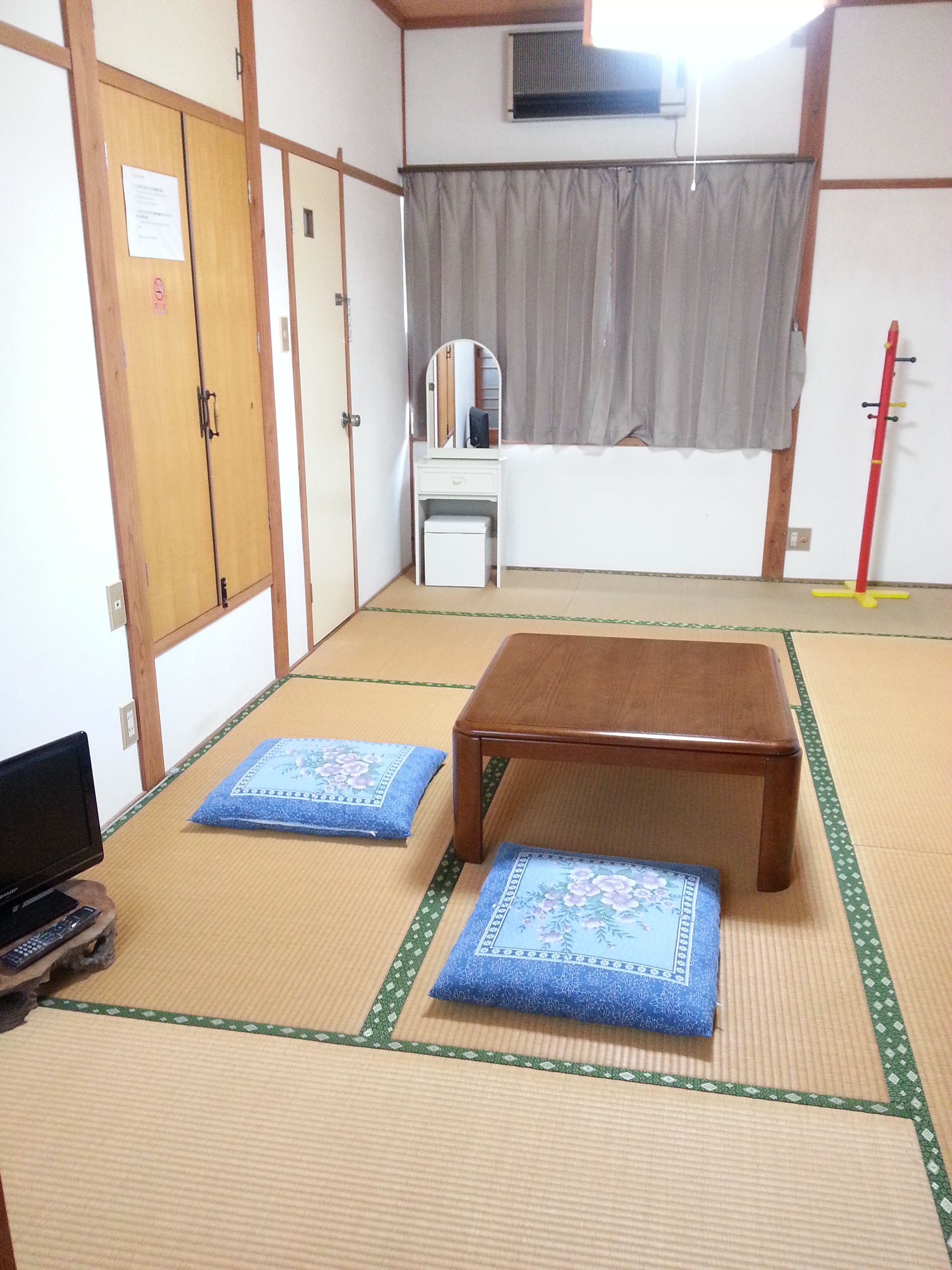 A traditional Japanese room with tatami flooring, a wooden table, a small desk with a mirror, and a futon bed.