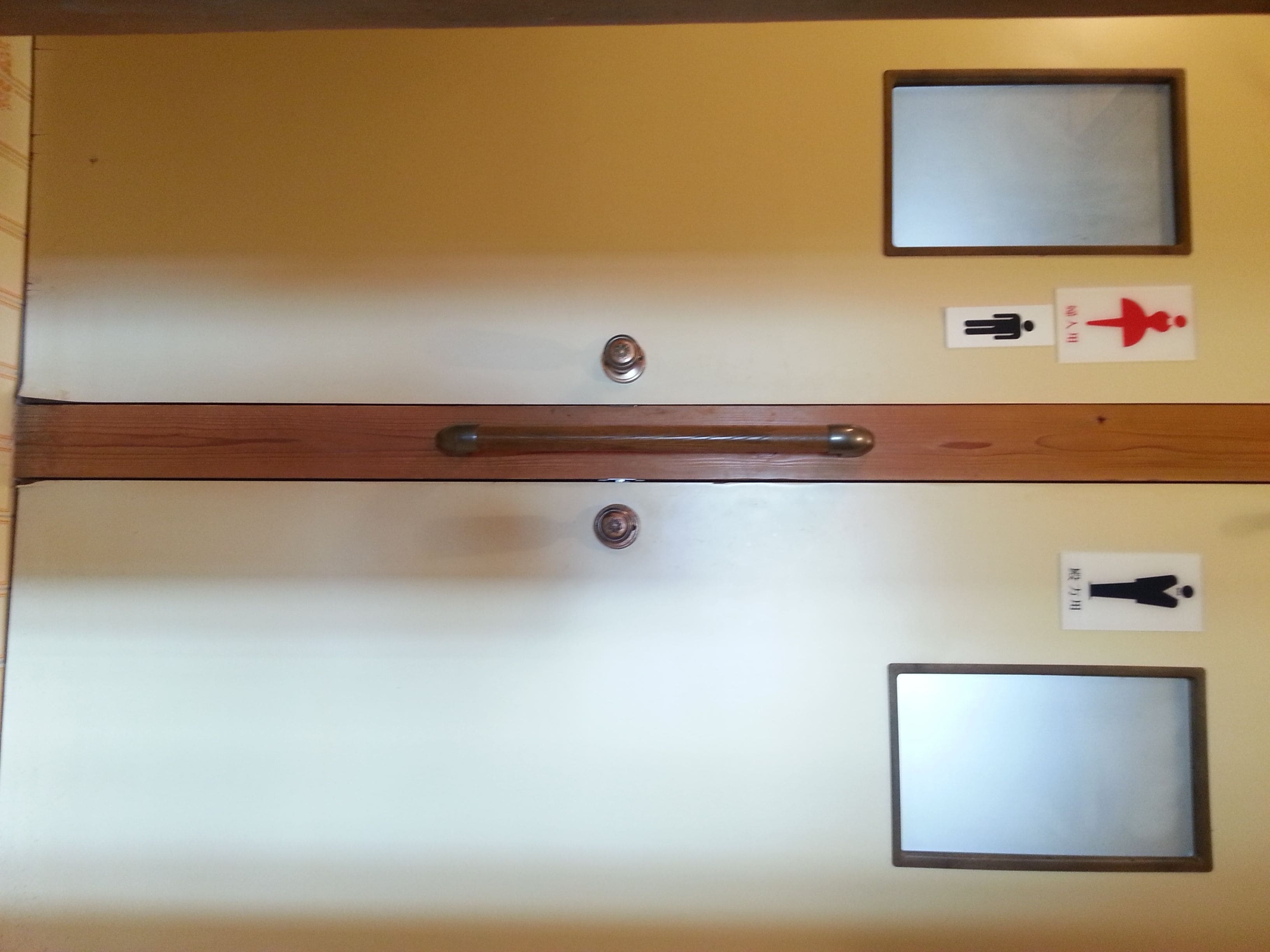 Una habitación de hotel con una puerta de madera, dos ventanas pequeñas y un espejo en la pared.
