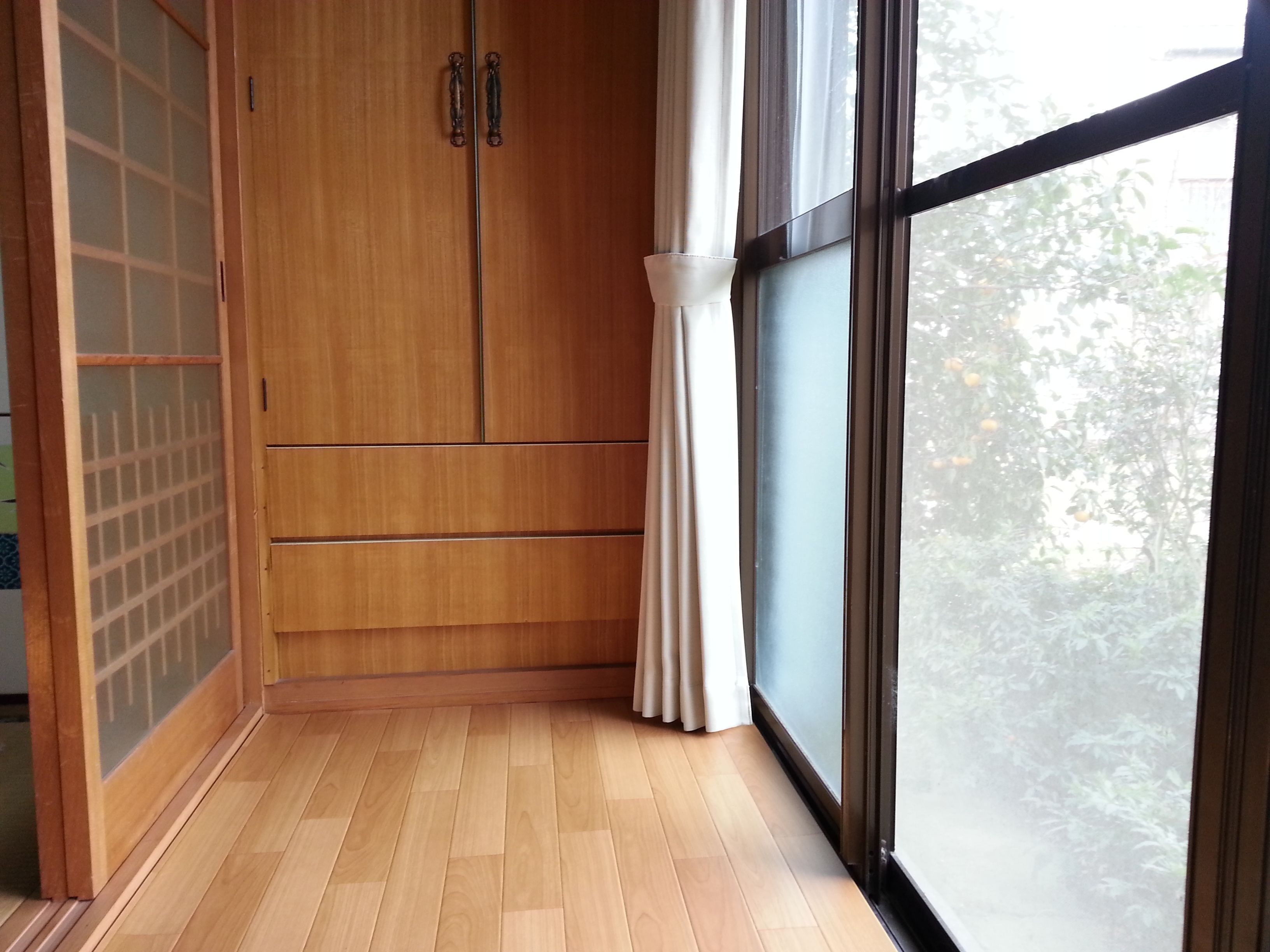 Habitación con suelo de madera, puerta corredera con diseño de cuadrícula y ventana grande con vistas a zonas verdes.