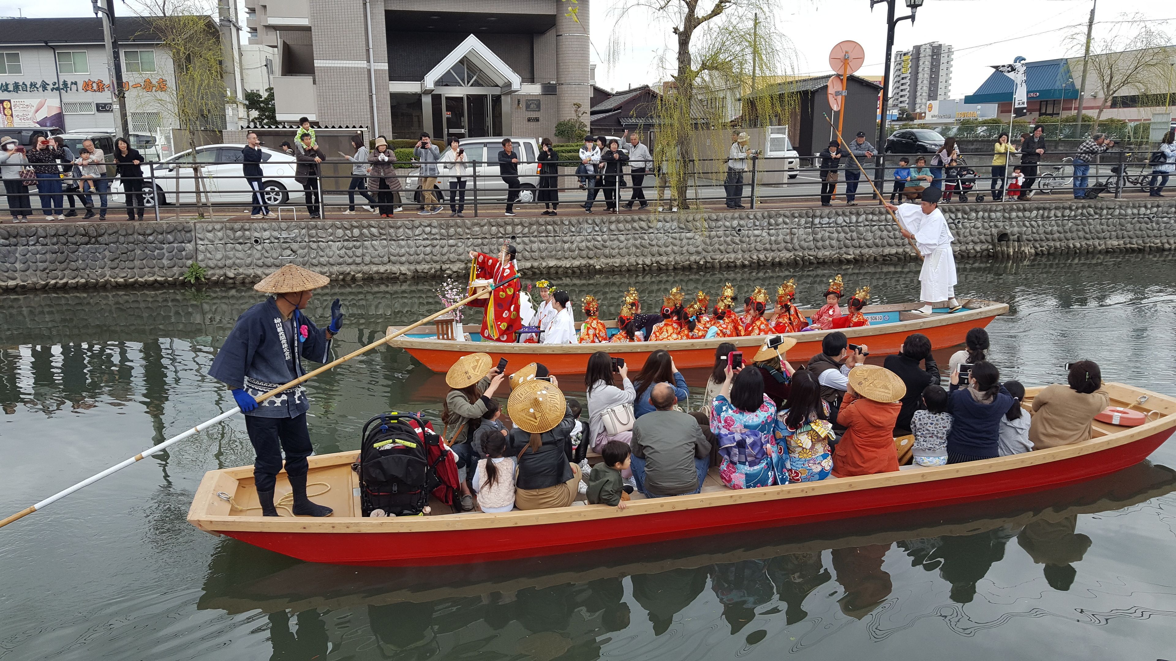 A traditional boat with passengers, a person rowing, and a crowd watching.
