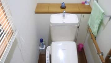 Ein kleines Badezimmer mit Toilette, Waschbecken und einem Holzregal darüber.