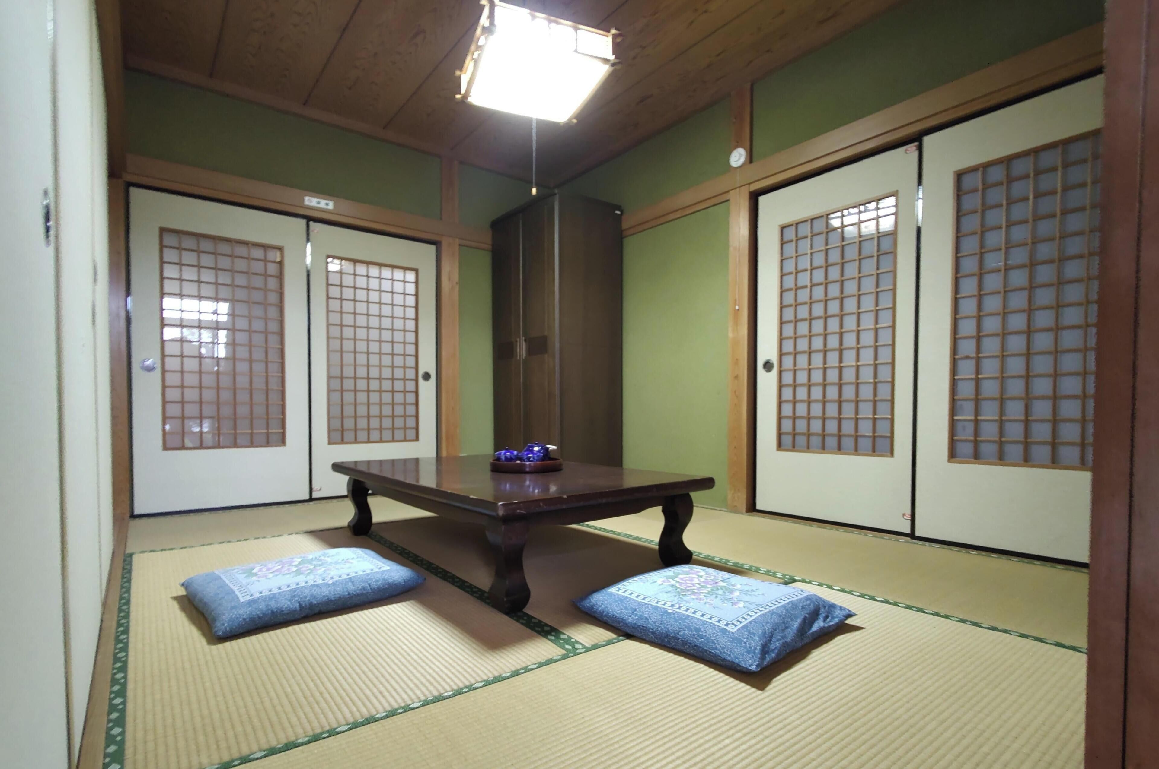 A traditional Japanese room with tatami flooring, a low table with cushions, and sliding doors with grid patterns.