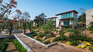 Una casa moderna con fachada de piedra, un patio con plantas en macetas y un jardín con diversas flores.