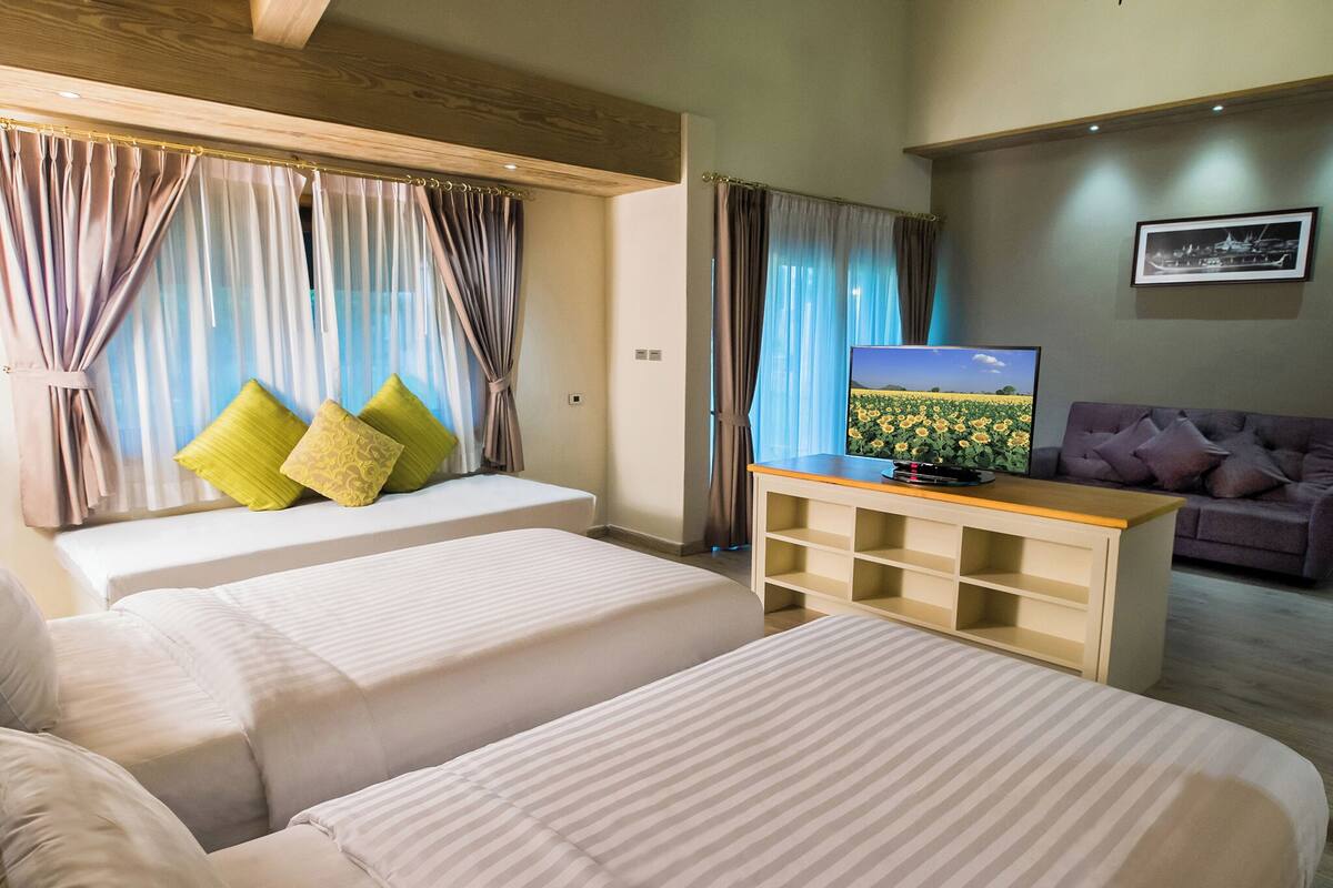 A hotel room with two beds, a TV on a wooden stand, and a couch.