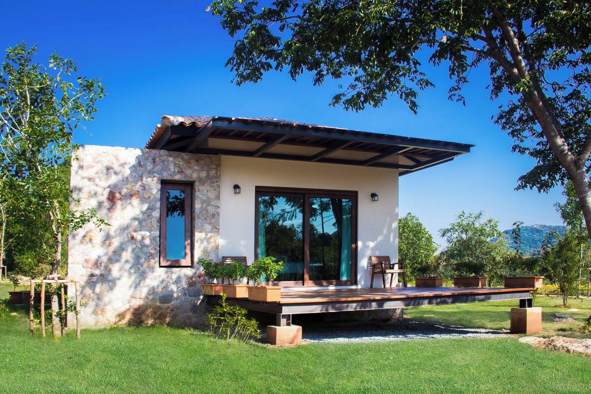 A modern house with a stone facade, large windows, and a deck with outdoor furniture.