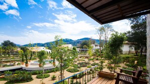 Una terraza de madera con barandilla que da a un jardín ajardinado con diversas plantas y una piscina.