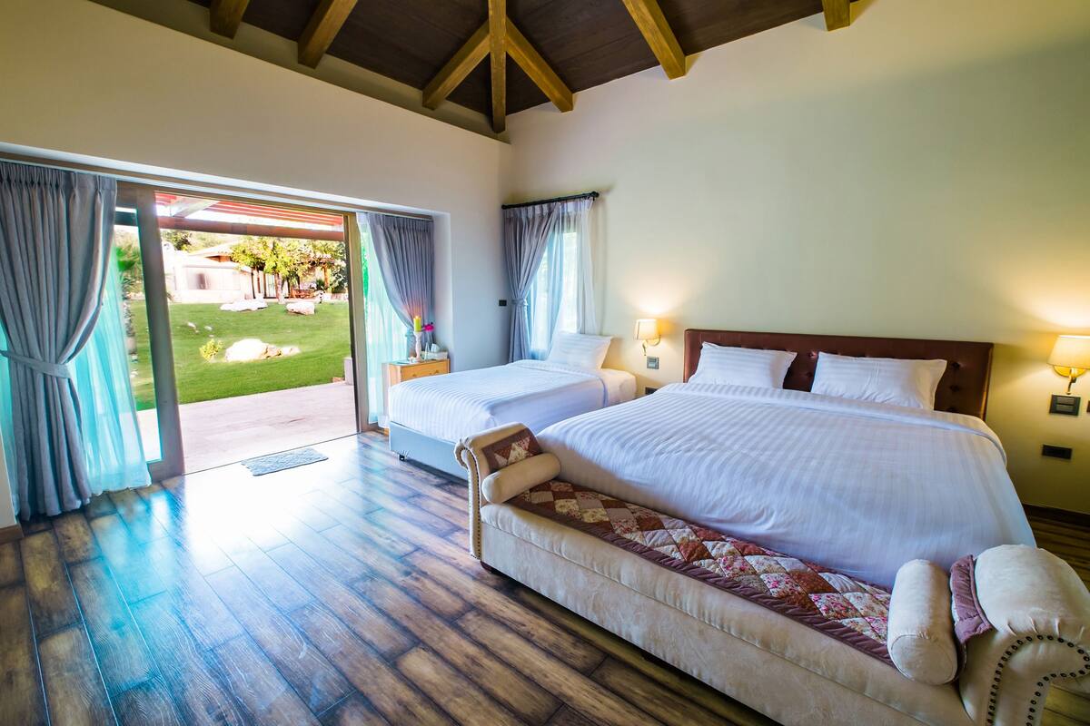 A bedroom with two beds, a sofa, and a view of a garden through an open door.