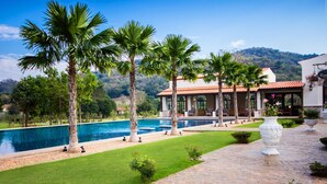 Un área junto a la piscina con palmeras, una piscina azul cristalina y un edificio con techo de tejas.