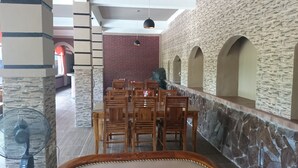 A dining area with wooden chairs and tables, stone walls, and a brick wall in the background. - Café Johan Home Stay Senggigi (Senggigi)
