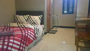 A bedroom with a bed, a bedside table, a chair, a window with blinds, and a door. - Café Johan Home Stay Senggigi (Senggigi)
