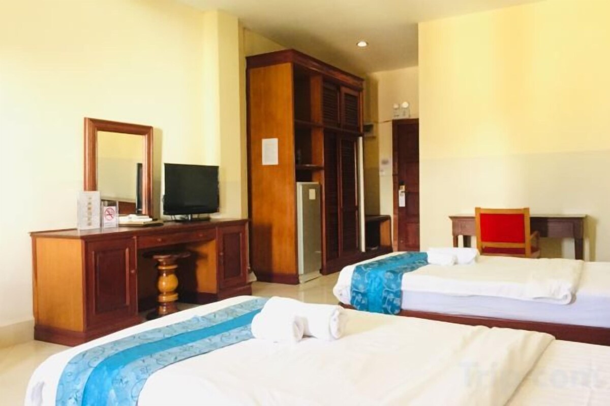 A hotel room with two beds, a television, a wardrobe, and a desk.