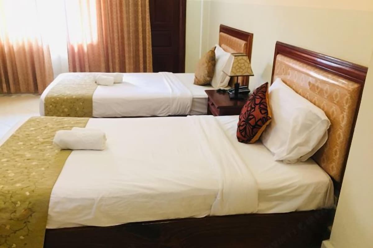 Ein Hotelzimmer mit zwei Betten, einem Nachttisch mit Lampe und einer Tür.