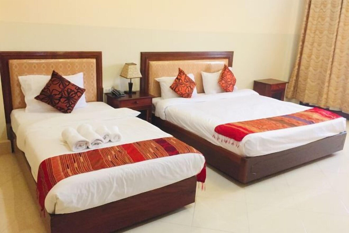 Dos camas dobles con cabeceros de madera, sábanas blancas y colchas estampadas en rojo y naranja.