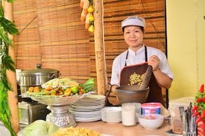 Een kok met een grote wok, omringd door verschillende soorten eten en kookgerei.