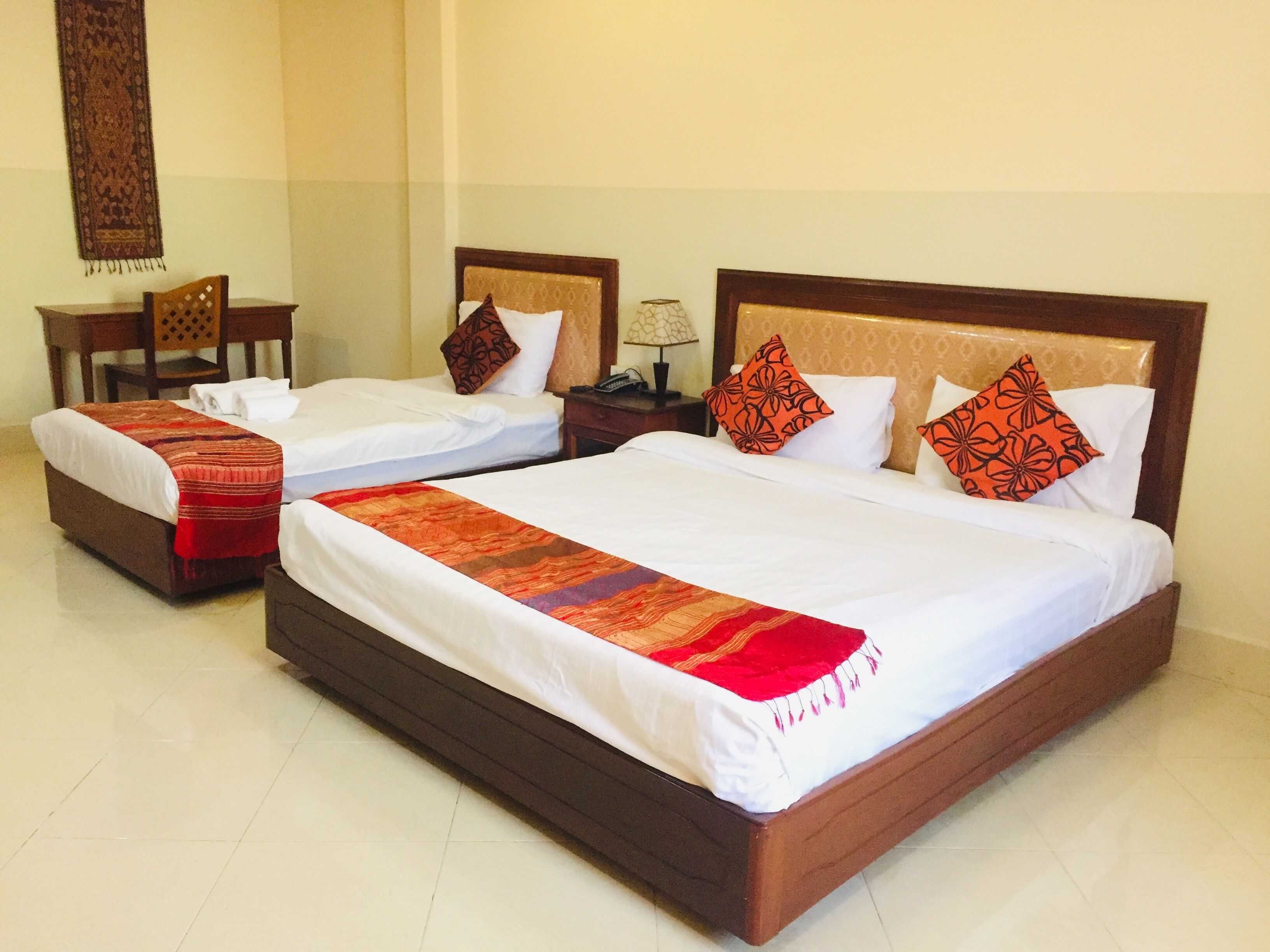 A hotel room with two single beds, a large bed, and a chair.