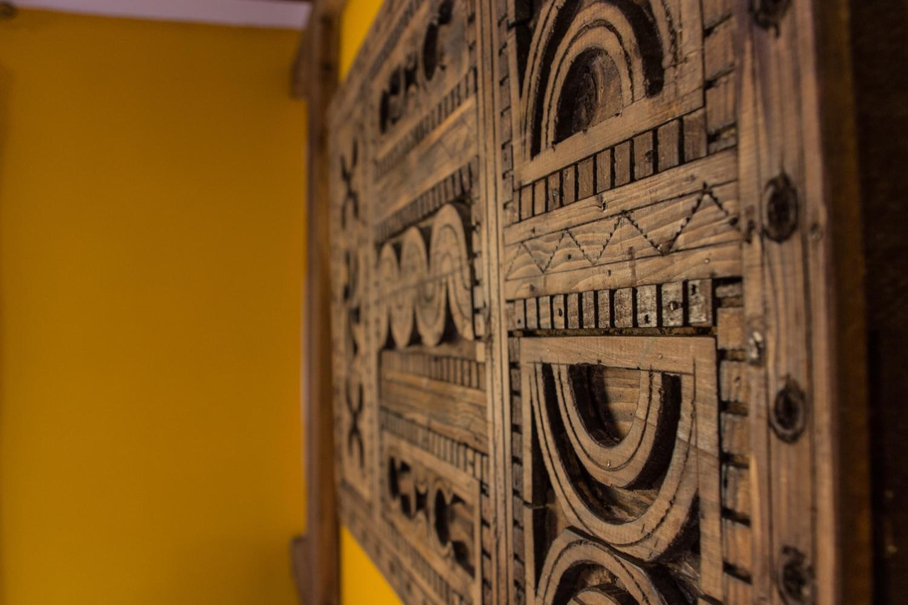 Primer plano de una puerta de madera con intrincados grabados y una pared amarilla al fondo.