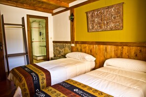 A room with two beds, a wooden ceiling, a stone wall, and a door leading to a shower area. - Hotel Plaza (Cuenca)