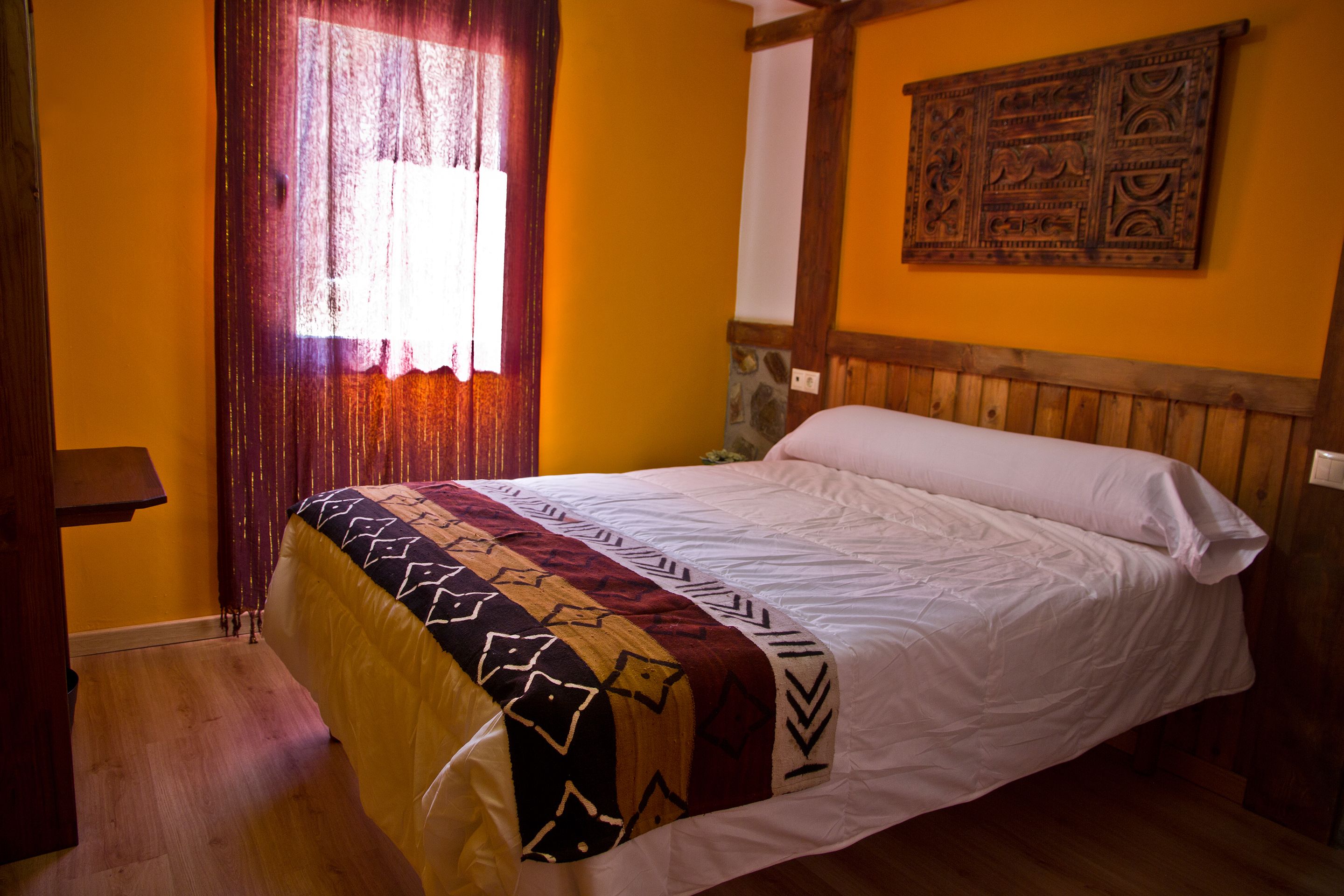 Un dormitorio con cabecera de madera, colcha estampada y ventana con cortinas.