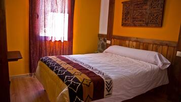 Un dormitorio con cabecera de madera, colcha estampada y ventana con cortinas.