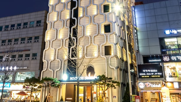 Un hotel moderno con una fachada geométrica singular, varios balcones y un área de entrada bien iluminada.