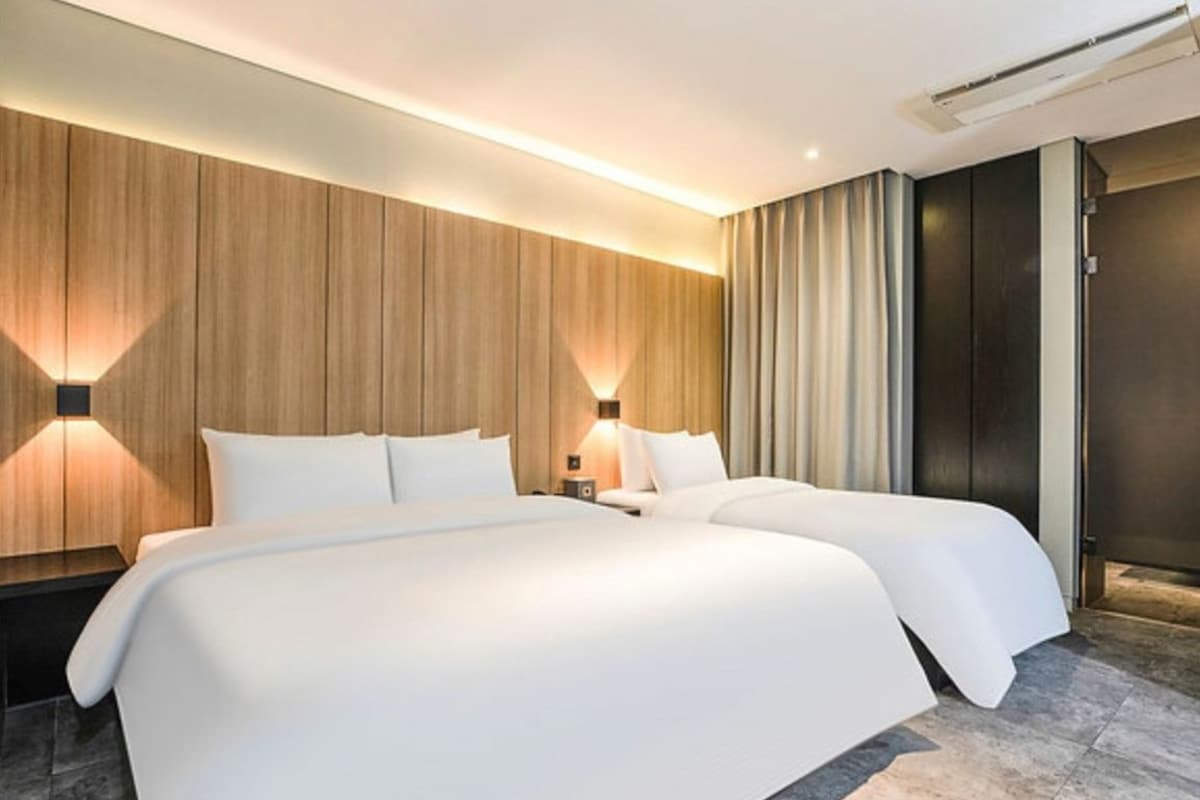Une chambre d’hôtel moderne avec deux lits, un mur décoratif en bois et une grande fenêtre avec des rideaux.