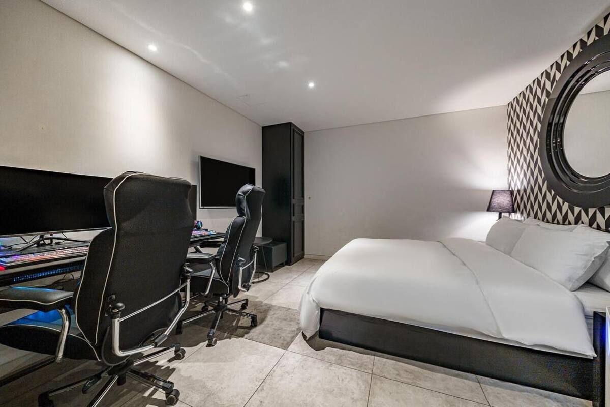 A modern hotel room with a large bed, a desk with a computer, and a large mirror on the wall.
