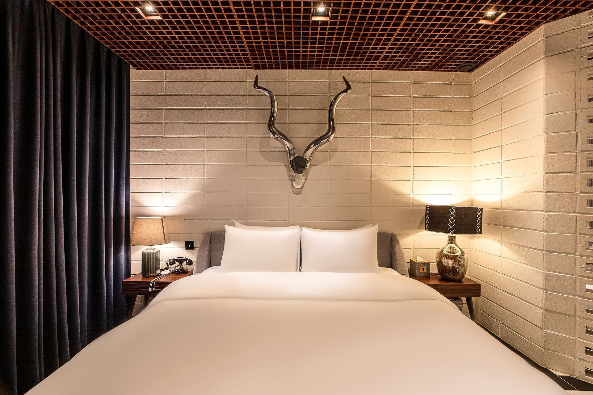Ein Hotelzimmer mit einem großen Bett, einem an der Wand befestigten Hirschskulptur und zwei Nachttischlampen.
