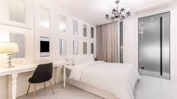 A modern bedroom with a white bed, a desk with a chair, a chandelier, and a sliding glass door.