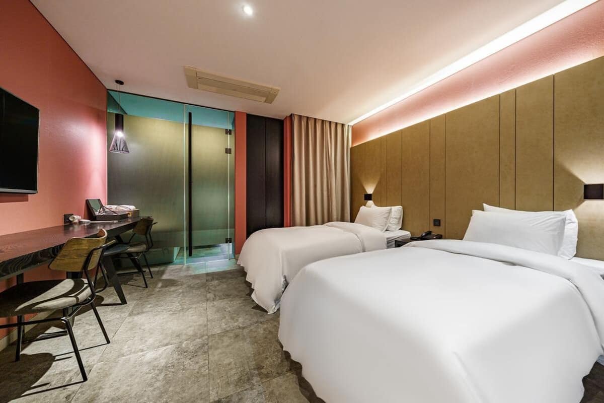 A hotel room with two beds, a desk, and chairs.