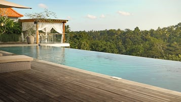 A wooden deck with an infinity pool overlooking a lush, green landscape.