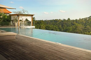 Una terraza de madera con piscina infinita que da a un paisaje verde y exuberante.