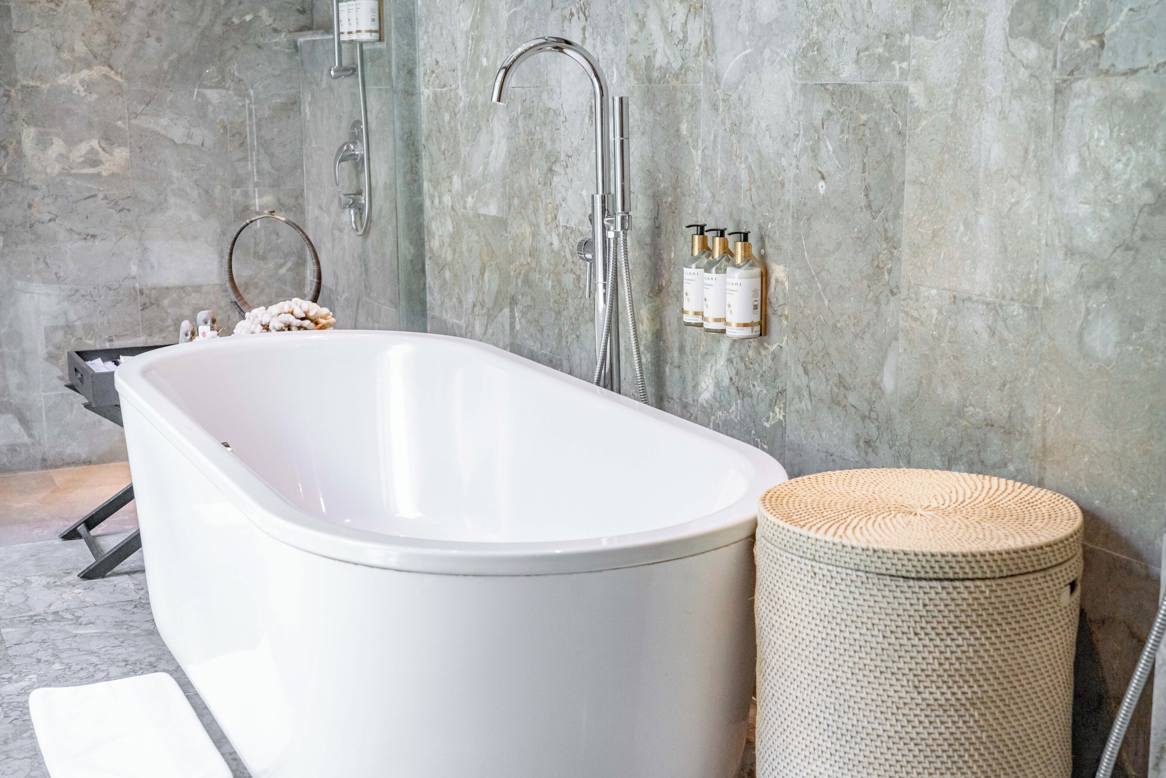 A modern bathroom with a freestanding bathtub, a showerhead, and a small wicker stool.