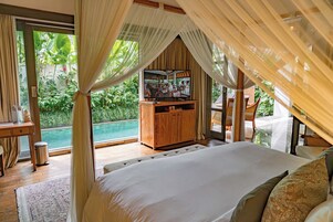 A bedroom with a large bed, a wooden cabinet, and a view of a swimming pool.