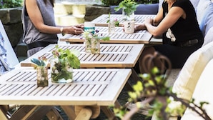 An outdoor patio with wooden tables and chairs, surrounded by greenery. - Okens Bed & Breakfast (Varberg)