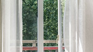 A chair with a striped blanket, a window with a view of greenery, and a balcony railing. - Okens Bed & Breakfast (Varberg)