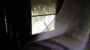 Una cama con mosquitero, una ventana con vistas a árboles y cortinas.