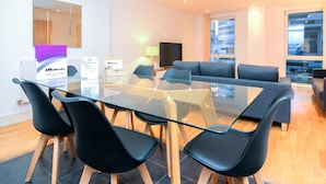 A modern hotel room with a glass dining table, black chairs, a grey sofa, and a TV. - Apartment Wharf - Indescon Wharf (London)