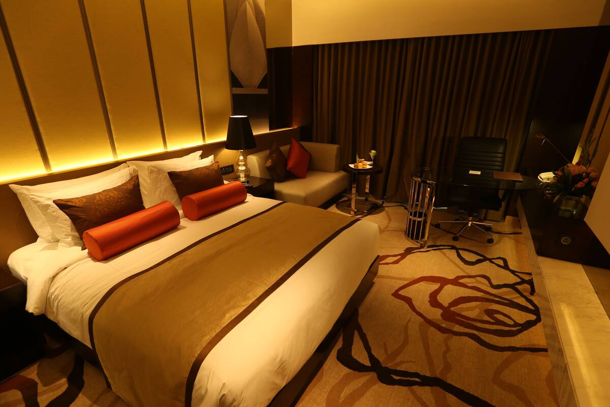 A hotel room with a large bed, a desk, a chair, a lamp, and a small table with a vase of flowers.