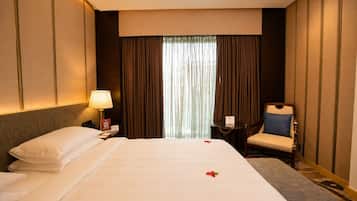 A hotel room with a bed, a chair, a desk, and a lamp.