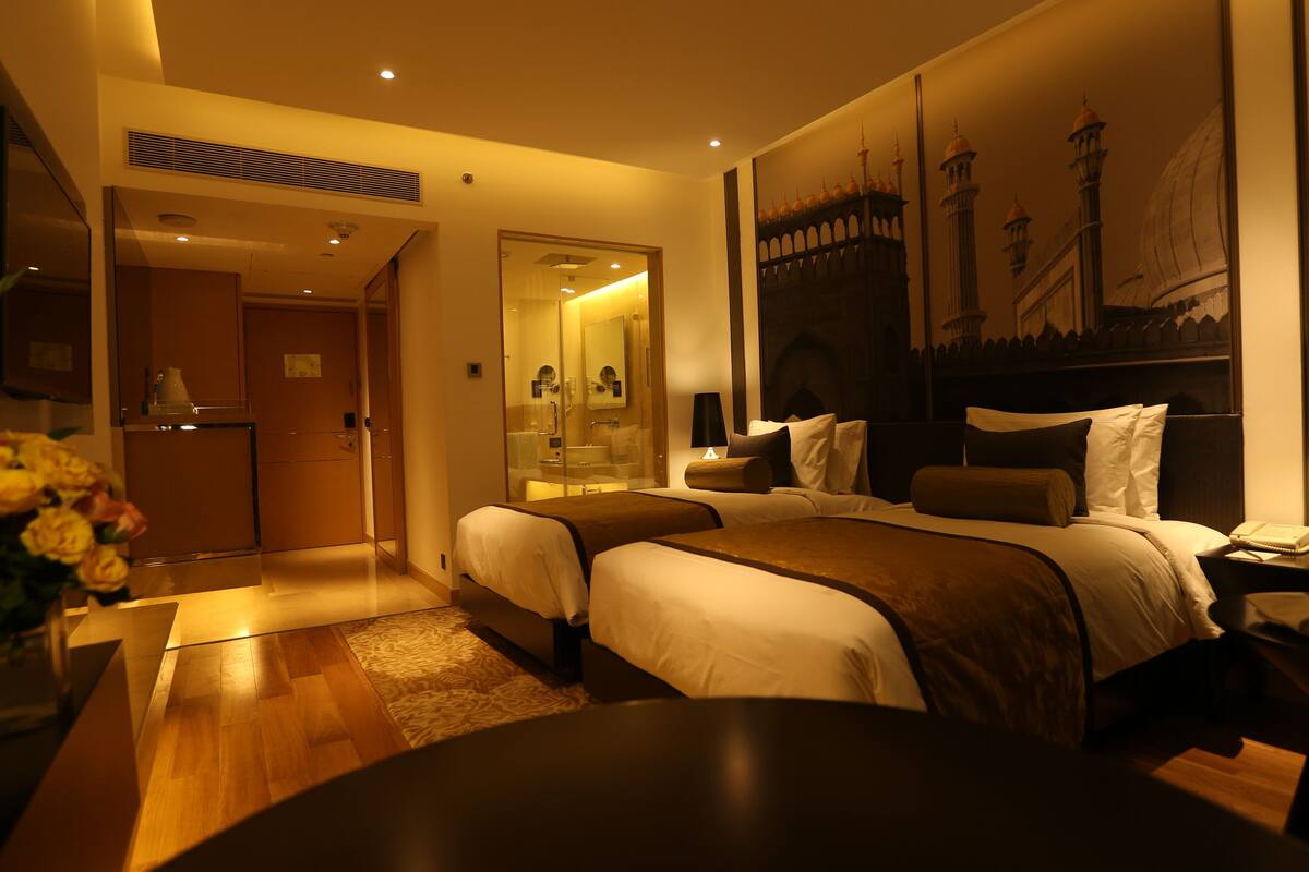 A hotel room with a large bed, a desk, a chair, a lamp, and a painting of a mosque on the wall.